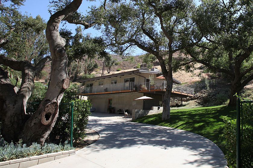 Curved driveway under mature oak trees leading to the home's railed deck