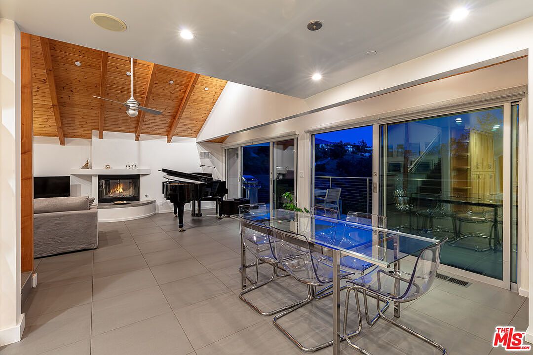 Open living and dining great room at twilight with vaulted wood ceiling, corner fireplace, and grand piano