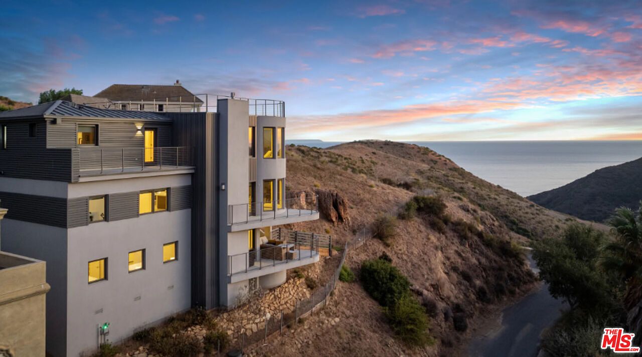 Contemporary three-story home perched on the canyon ridge at dusk with windows glowing above the Pacific