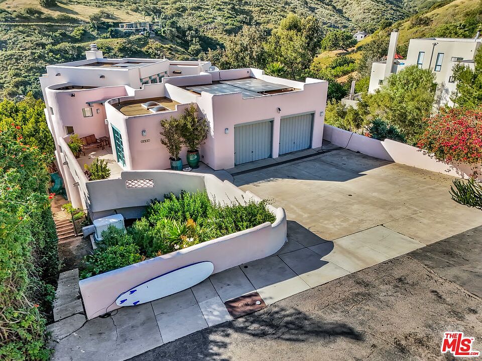 Pink stucco residence with a rooftop deck, surfboard resting against the entry garden wall
