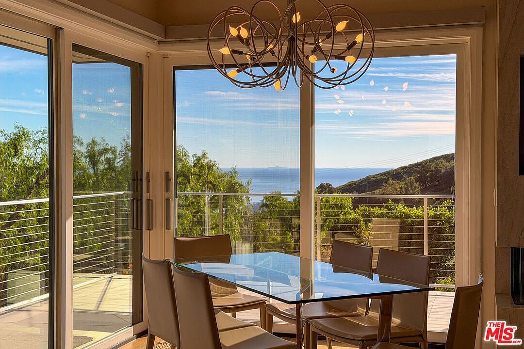 Breakfast nook with an iron-leaf chandelier and floor-to-ceiling windows framing the ocean horizon