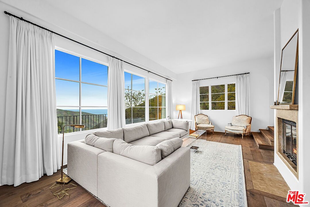 White-walled great room with a sectional sofa, tall windows opening onto the canyon, and a corner fireplace