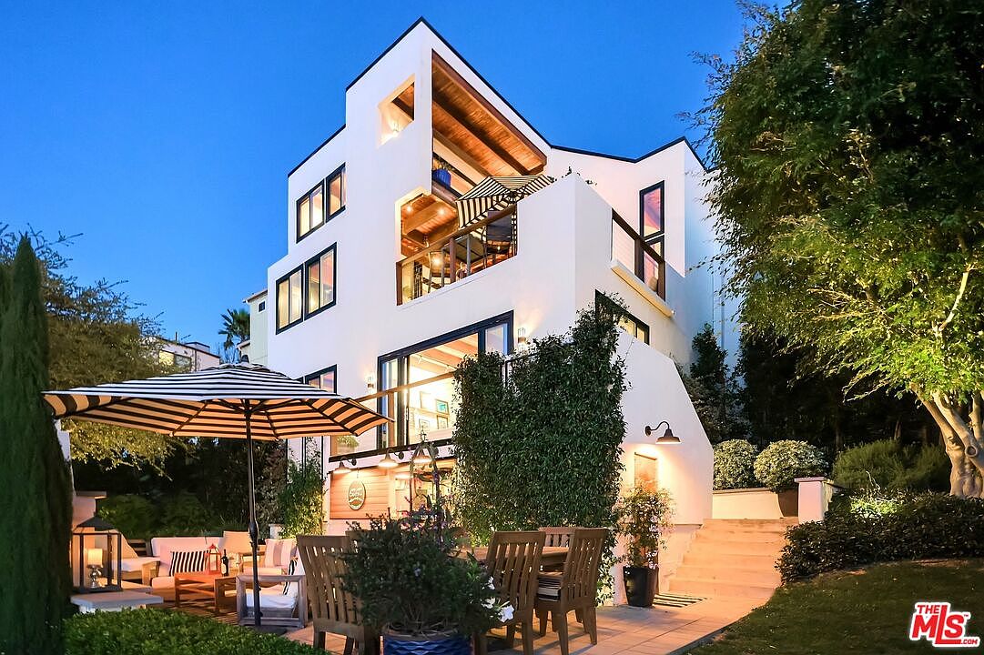 Rear elevation of the home at dusk with a striped umbrella shading the dining patio and tiered windows lit from within
