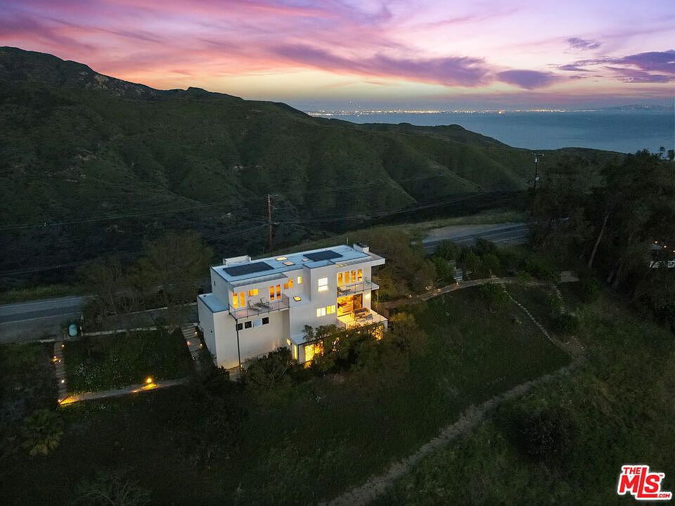 Twilight aerial of 2727 Corral Canyon, a modern hillside home above the Pacific with the lights of Santa Monica twinkling across the bay